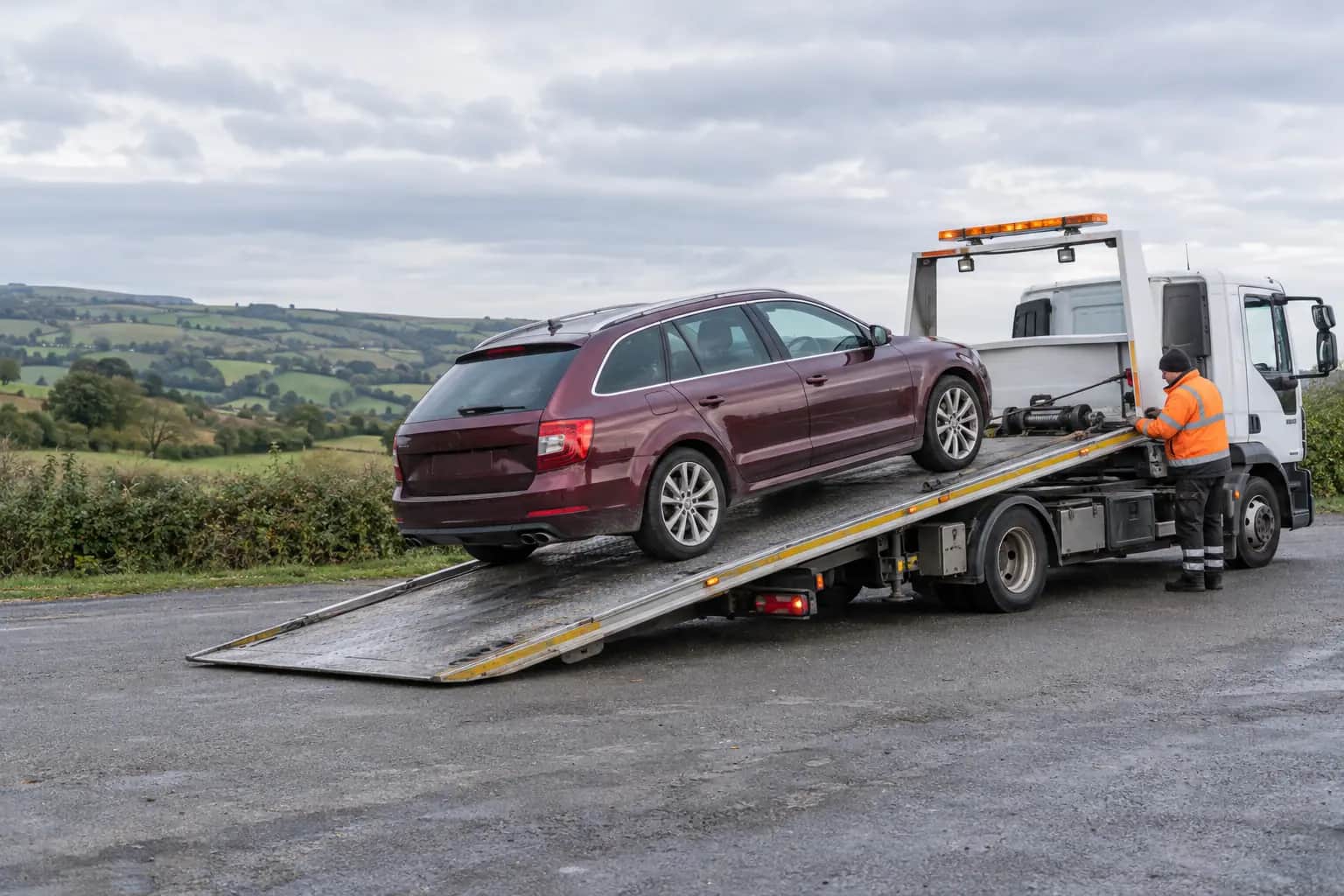 Car loaded onto a flatbed recovery truck on a rural road near the A68, rolling hills behind