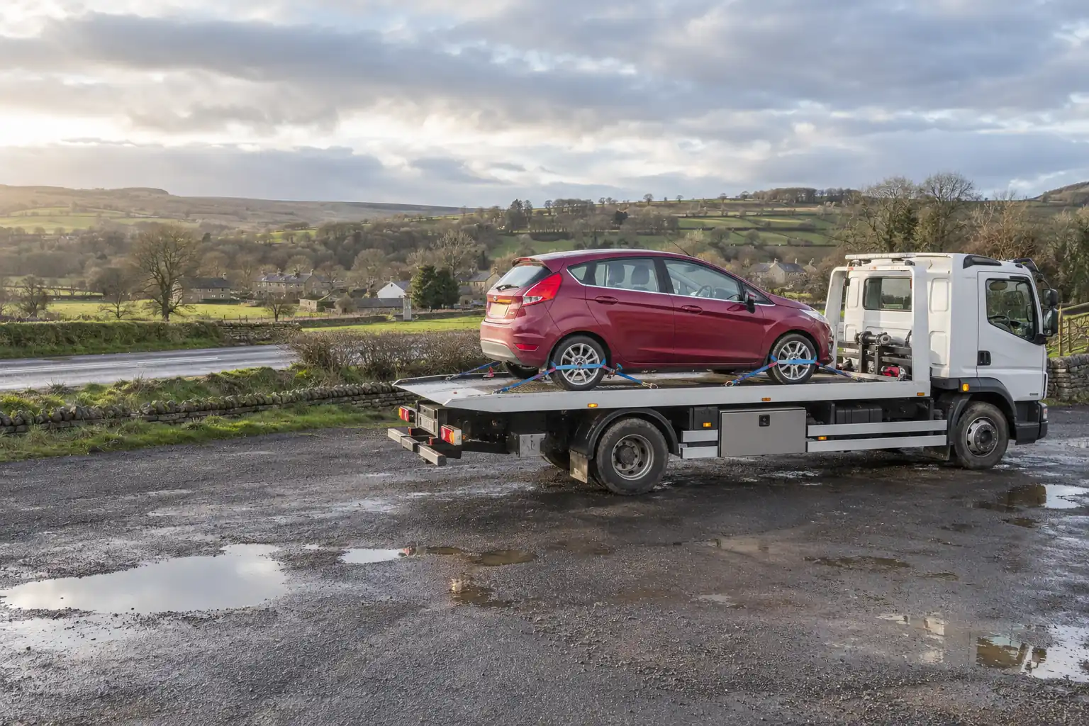 Car on a flatbed recovery truck with a Teesdale village in the valley below